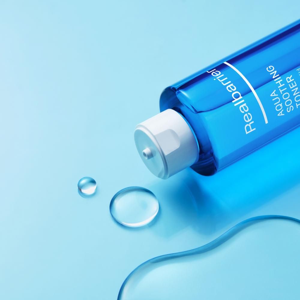 Blauwe fles ligt. Daarnaast waterdruppels. Opschrift: Realbarrier, AQUA SOOTHING TONER.