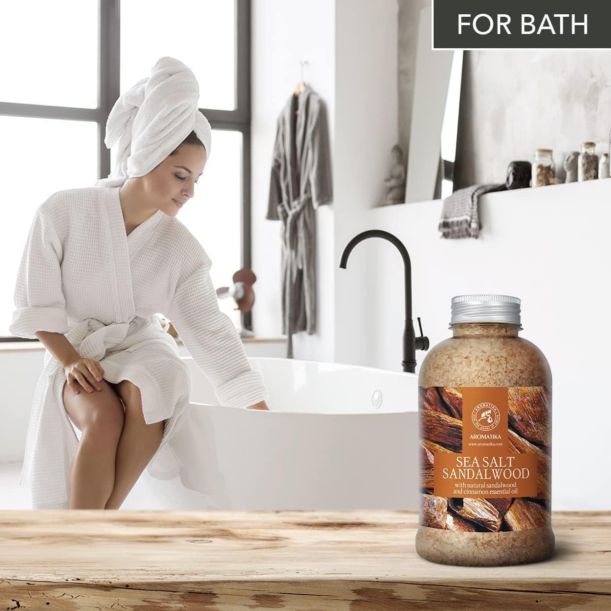 Femme en peignoir au bord d'une baignoire avec sel de bain AROMATIKA bois de santal à côté.