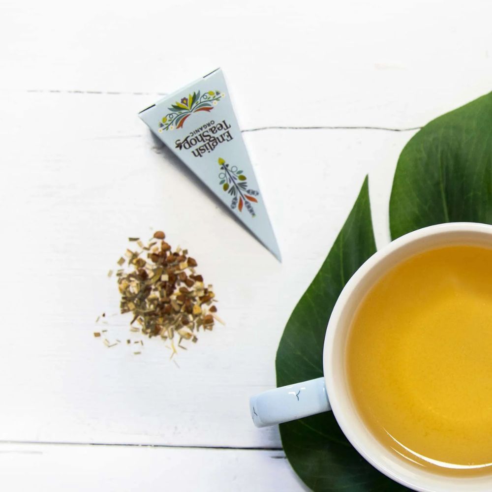 Theezakje met losse blaadjes naast een kopje thee. Piramidevormige verpakking. Opschrift: English Tea Shop Organic.