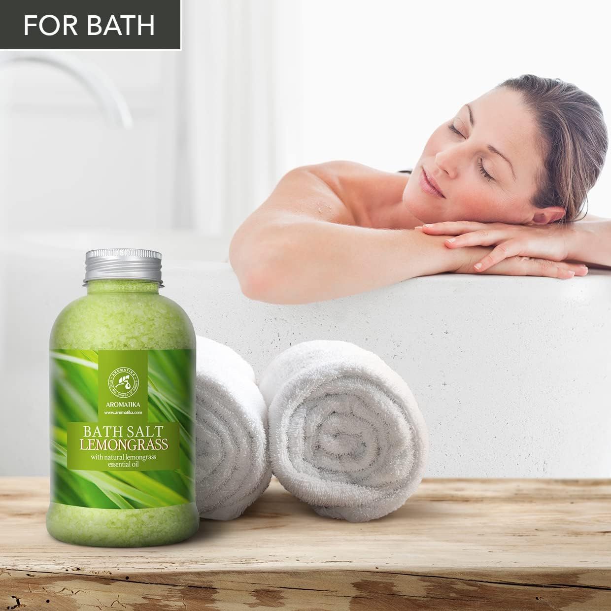 Femme se détendant dans une baignoire à côté d'AROMATIKA Sel de bain Lemongrass. Deux serviettes roulées à côté.