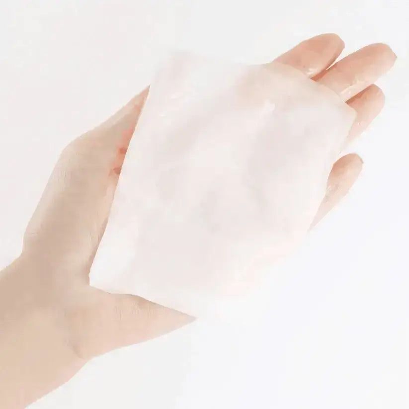 Masque en tissu hydratant tenu dans une main. Forme rectangulaire, blanc, légèrement transparent.