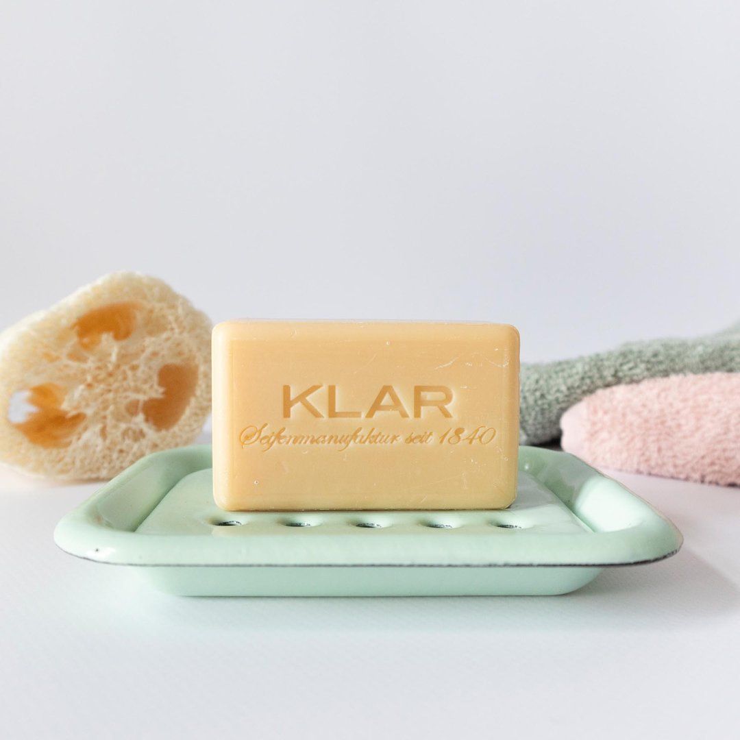 Savon sur porte-savon en émail menthe. Inscription Klar sur le savon. Porte-savon avec luffa et serviettes.