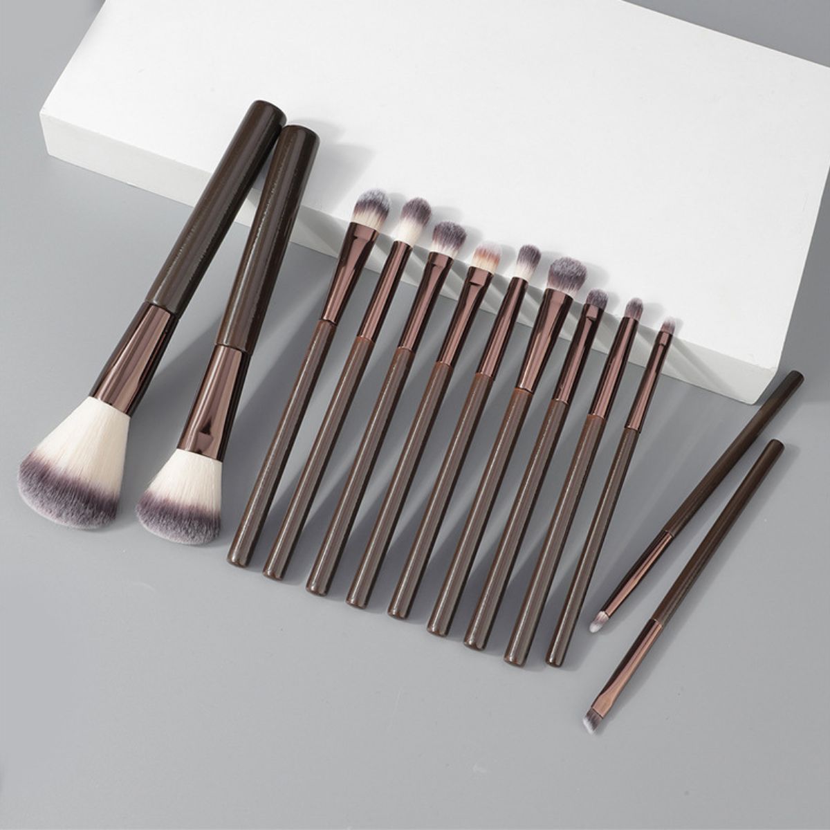 Un ensemble de 12 pinceaux de maquillage foncés avec des poils blancs et gris.