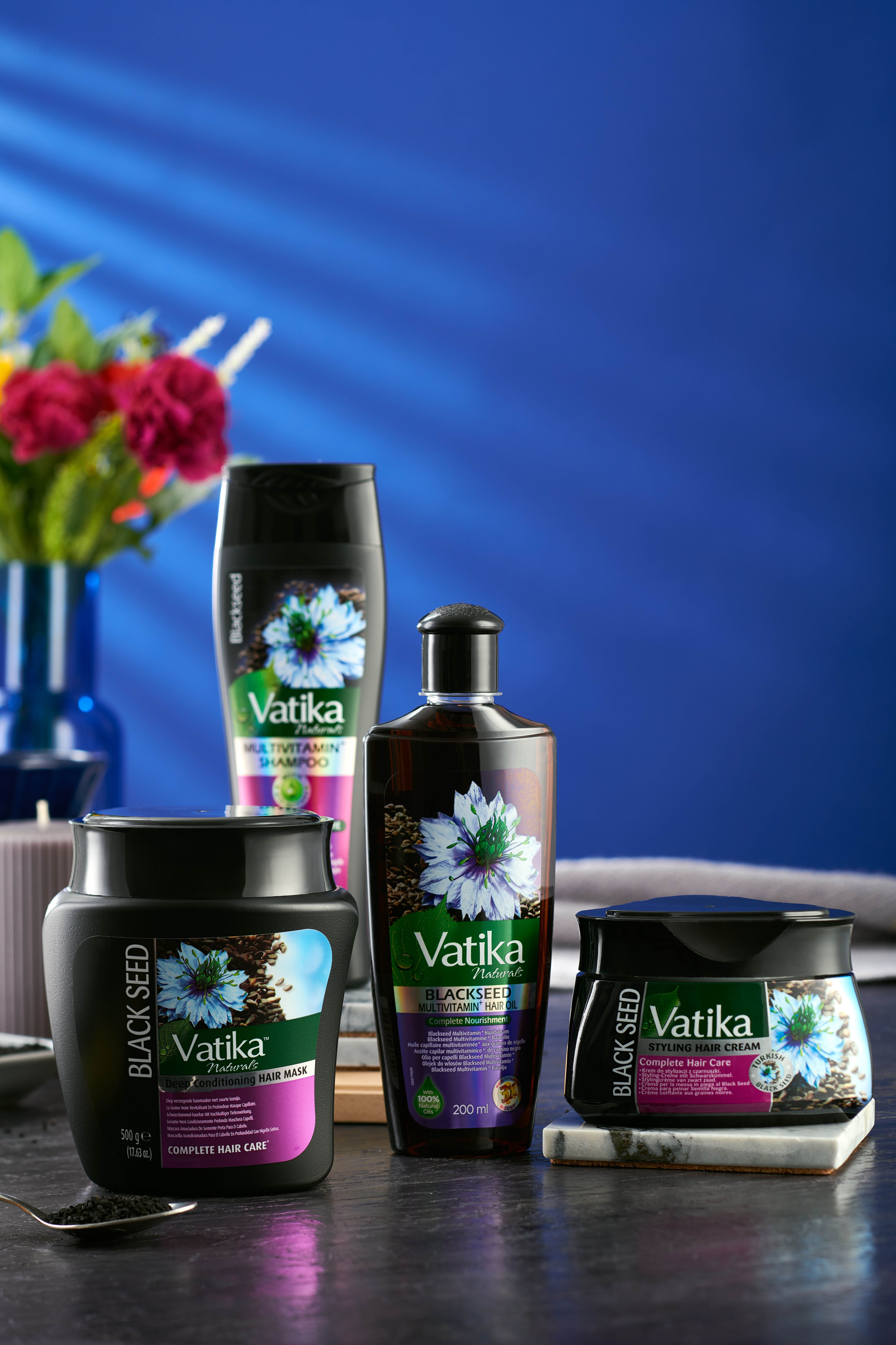 Verschillende Vatika Naturals Schwarzkümmel producten. Flessen en potten op blauwe achtergrond, met bloemen.