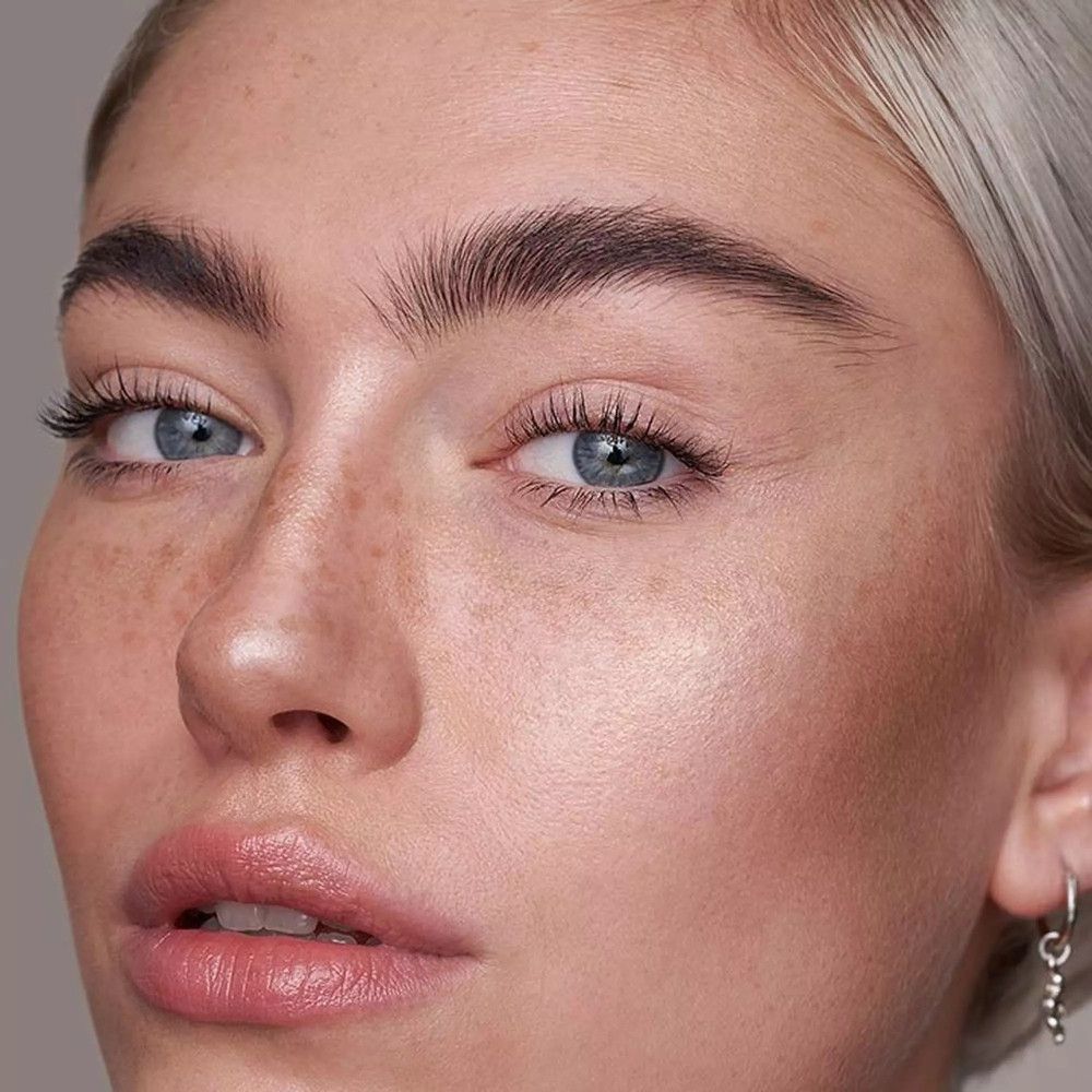 Close-up van een gezicht met blauwe ogen, blond haar en sproeten. De huid heeft een natuurlijke glans.