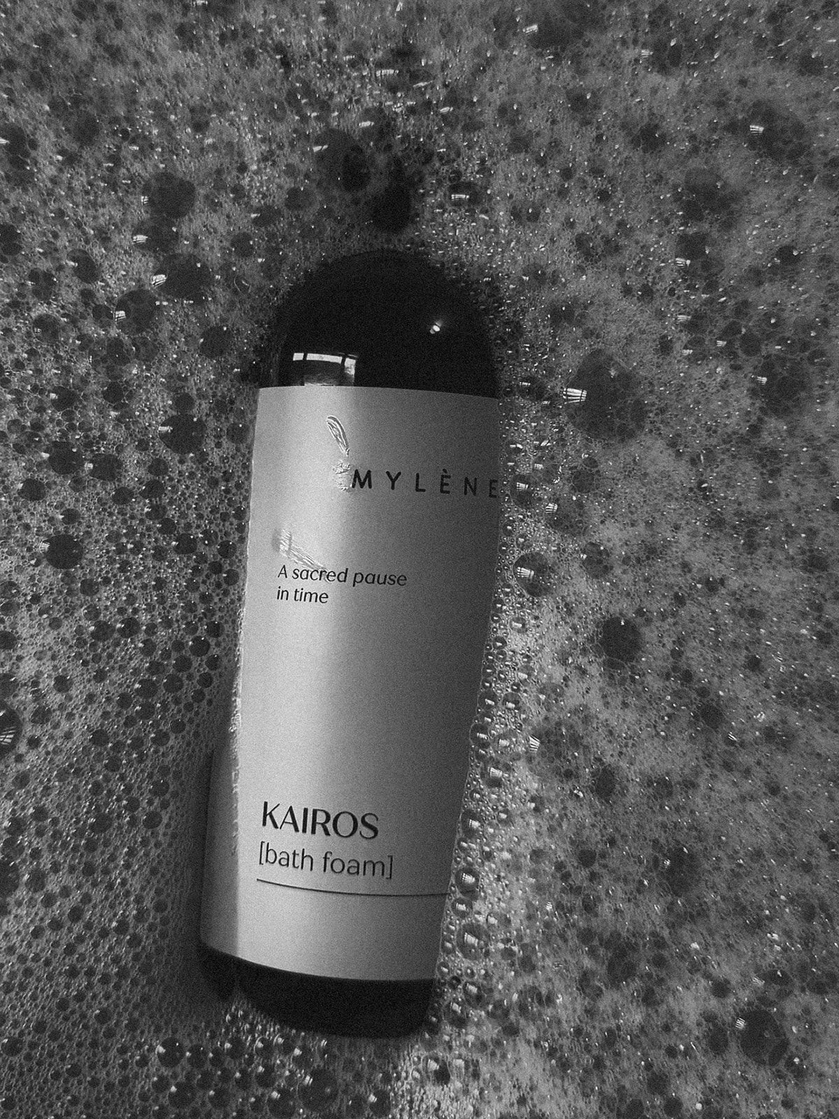 Pompfles met licht etiket "KAIROS [Bath foam]" in een bubbelbad.