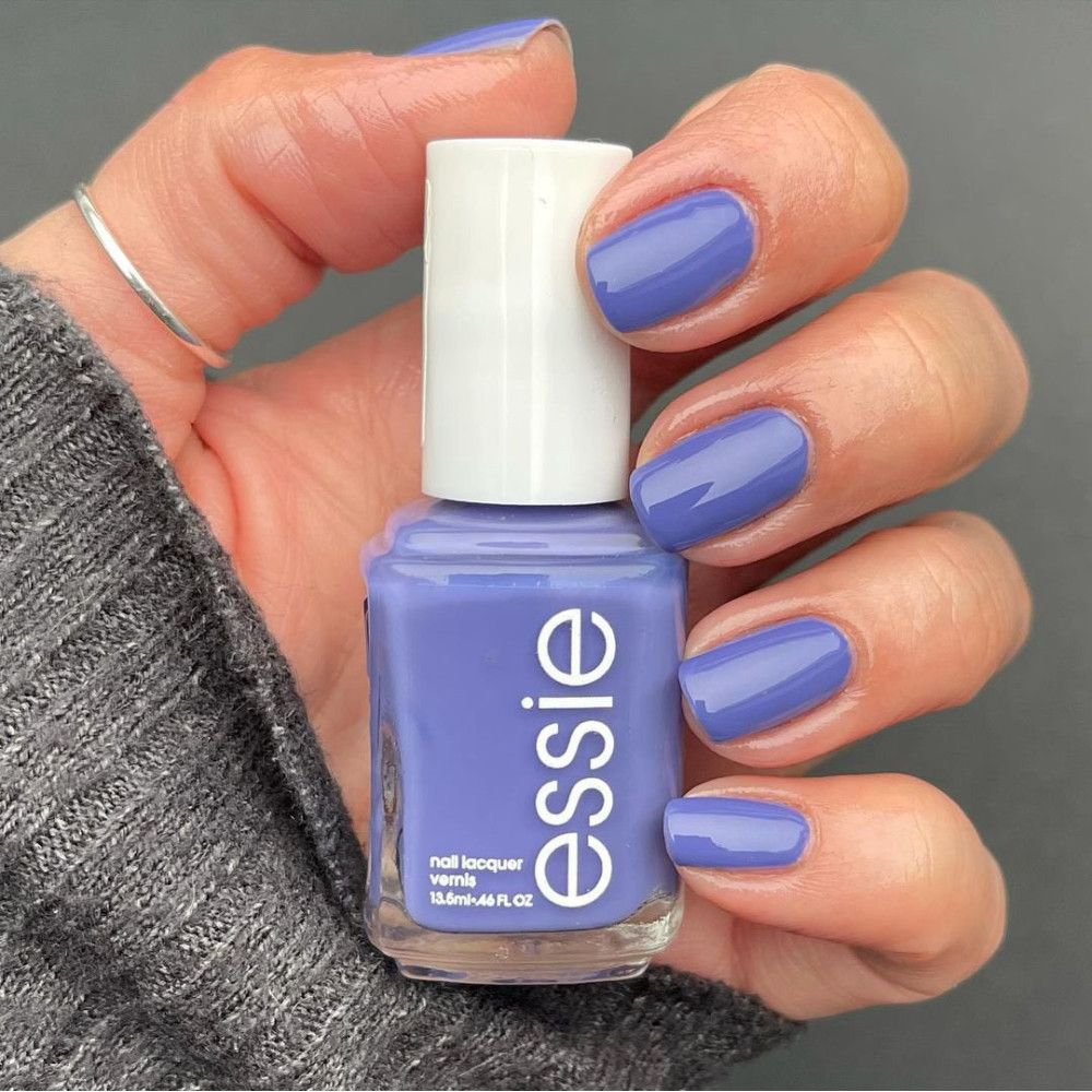 Essie nagellak in lichtblauw op nagels aangebracht. Flesje naast hand. Merknaam "essie" zichtbaar.