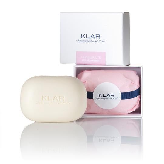 Ovale, lichtbeige zeep. In witte doos met roze papier en blauwe band. Klar-logo zichtbaar.