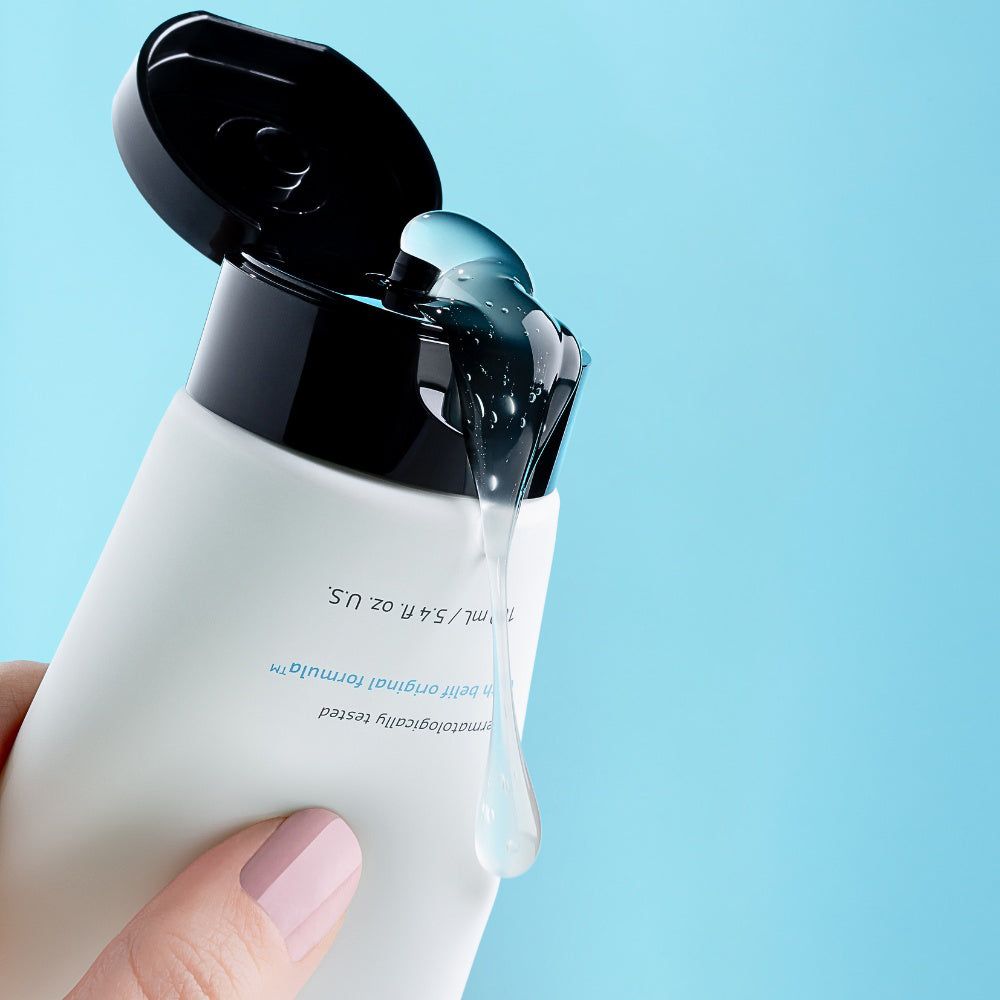 Main pressant un tube, gel transparent coulant du bouchon ouvert.