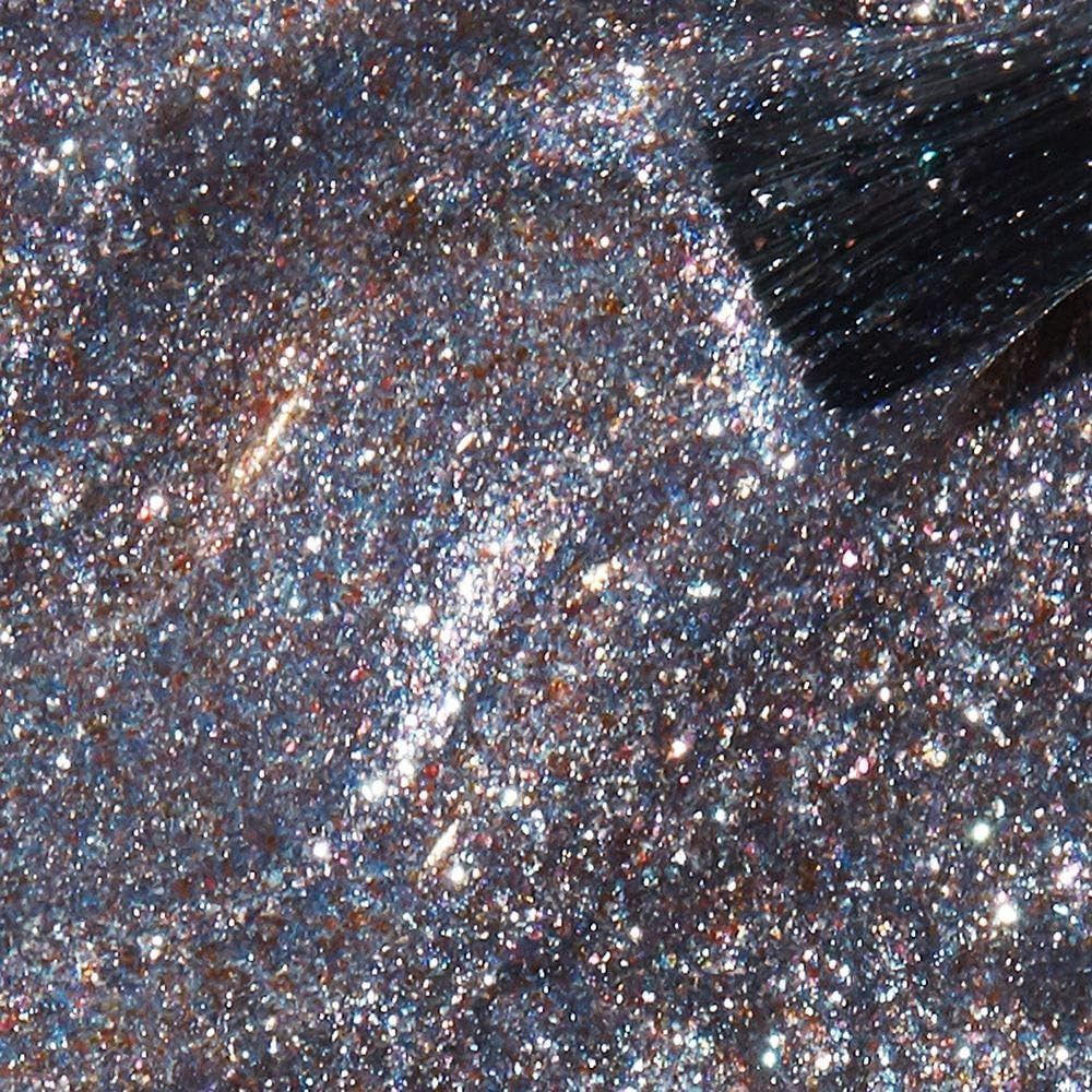 Gros plan sur du vernis à ongles pailleté. Un pinceau touche la surface. Le vernis est argenté avec des particules scintillantes.