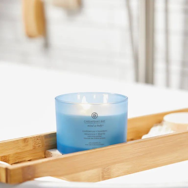 Bougie bleue Chesapeake Bay, 3 mèches, sur plateau en bois. Texte: confidence + freedom, assurance + liberté. Contexte salle de bain.