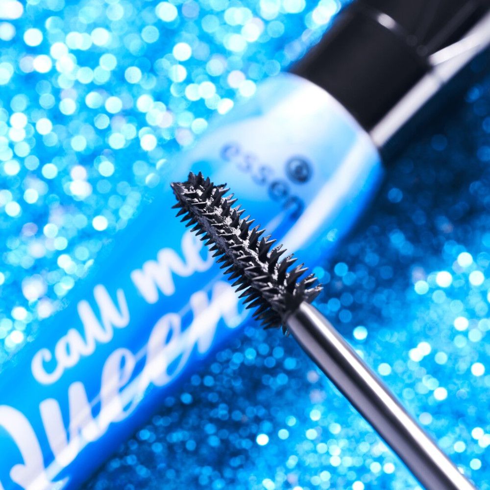 Gros plan sur la brosse et le tube de mascara. Paillettes bleues en arrière-plan. Nom du produit visible.