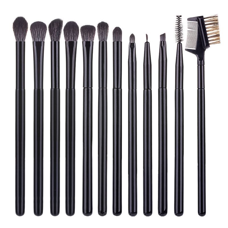 Onze pinceaux noirs pour fard à paupières et sourcils, alignés sur une surface blanche, avec un peigne et une brosse.