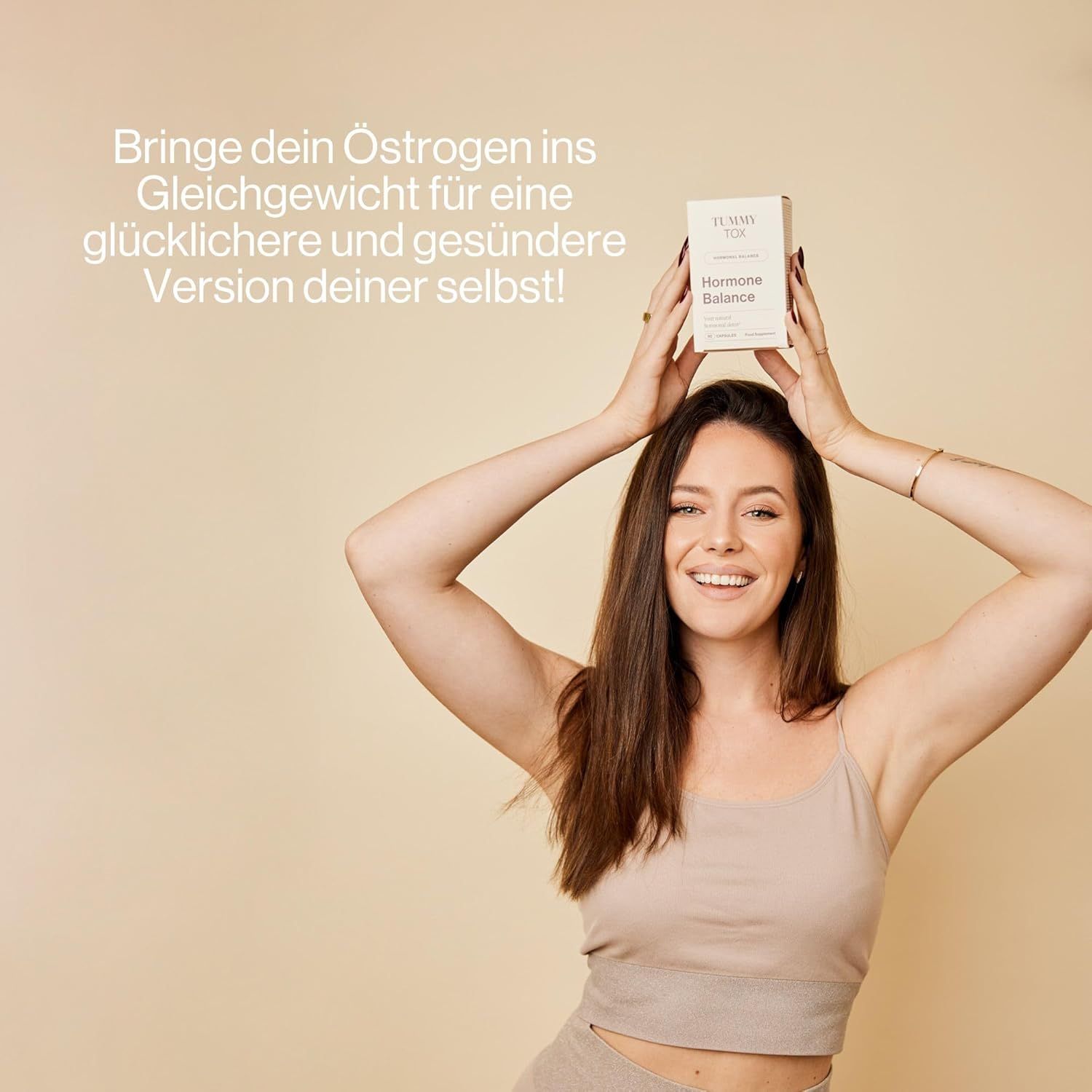 Femme tenant une boîte "Tummy Tox Hormone Balance" au-dessus de sa tête.