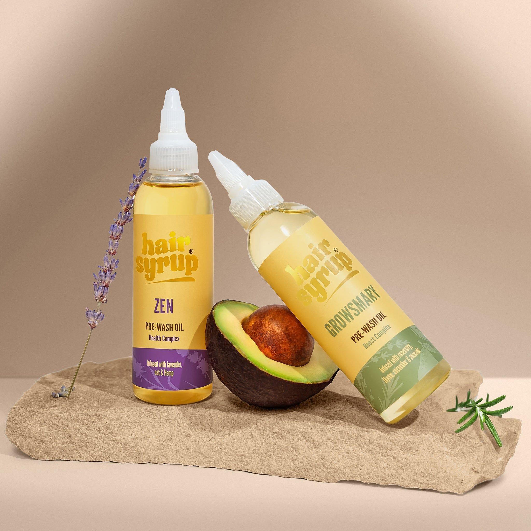 Deux flacons de liquide jaune avec étiquettes. Un flacon est incliné contre un avocat. Lavande et pierre en arrière-plan.