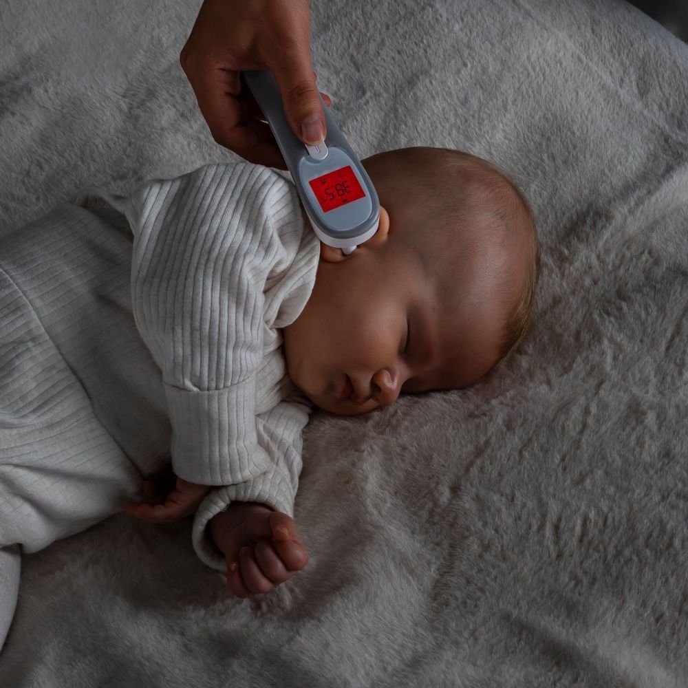 Bébé avec thermomètre auriculaire. Affichage : 36,5°C. Thermomètre gris.