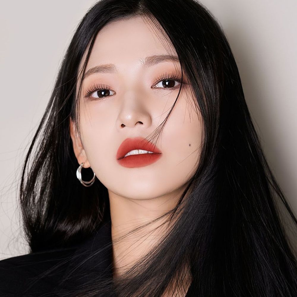 Portrait d'une femme aux cheveux noirs et au rouge à lèvres. Le rouge à lèvres est brun-rouge. Elle porte un blazer noir.