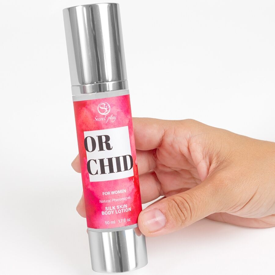 Hand houdt een Secret Orchid Body Lotion flesje vast. Zilverkleurig flesje met rood etiket.