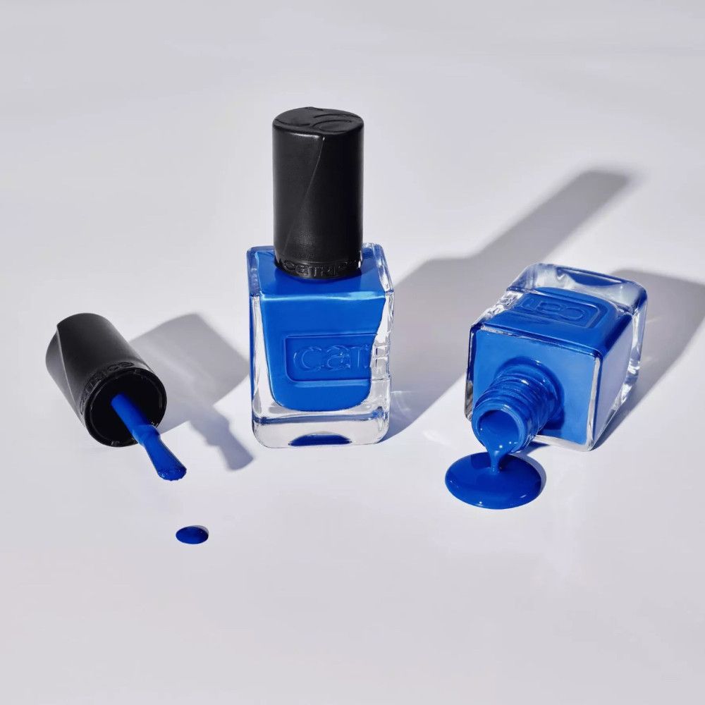 Trois flacons de vernis à ongles bleus, un ouvert, un renversé. Marque Catrice visible.