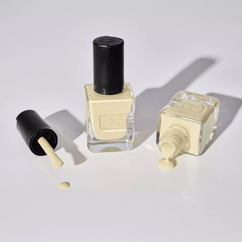 Trois flacons de vernis à ongles sur fond blanc. Un flacon est couché, du vernis a coulé. Deux flacons sont debout.