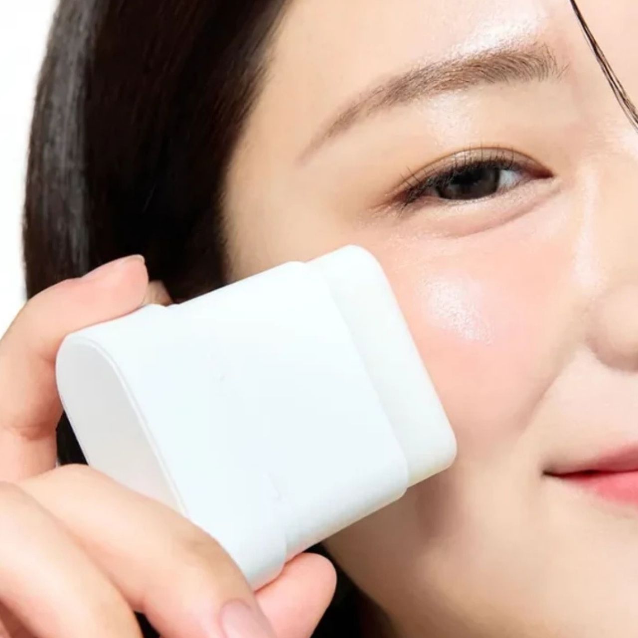 Une femme applique le SOME BY MI PDRN Spirulina Poreless Primer sur sa joue avec un applicateur blanc.