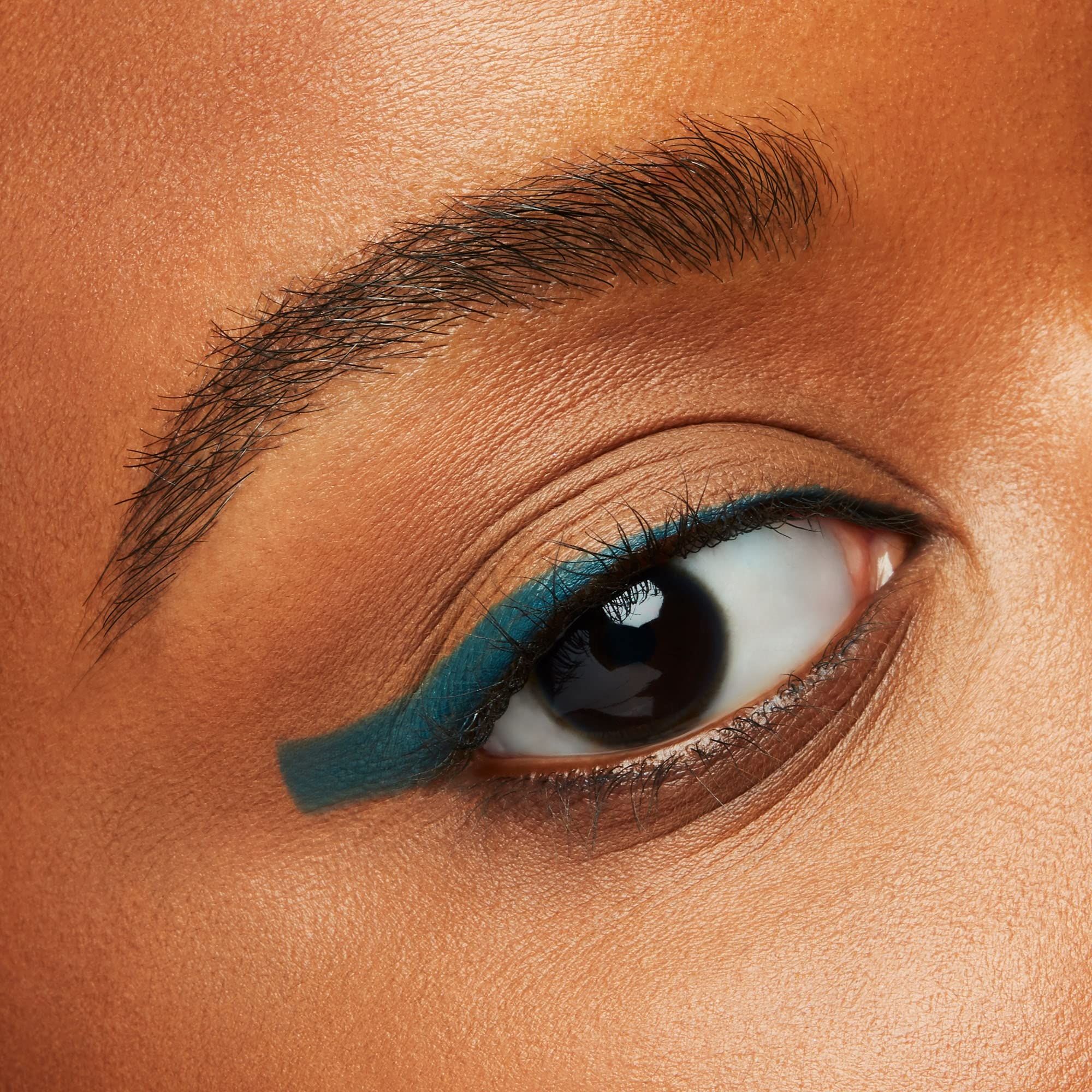 Gros plan sur un œil avec Shiseido Eye Microliner Ink 08 en Teal sur la paupière supérieure. Peau et sourcils bruns.