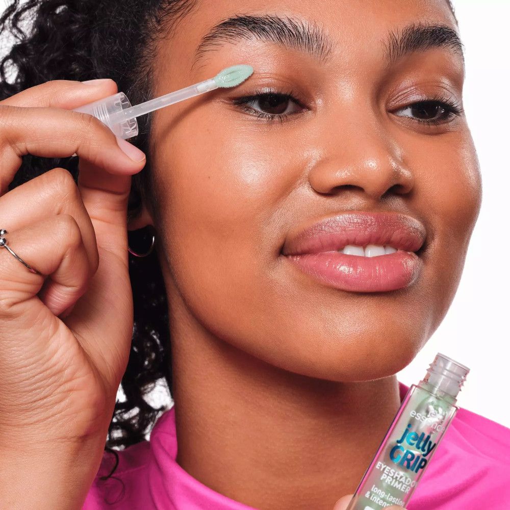 Femme appliquant la base de fard à paupières Essence Jelly Grip. Produit et applicateur visibles. Texte : Jelly Grip, Eyeshadow Primer.