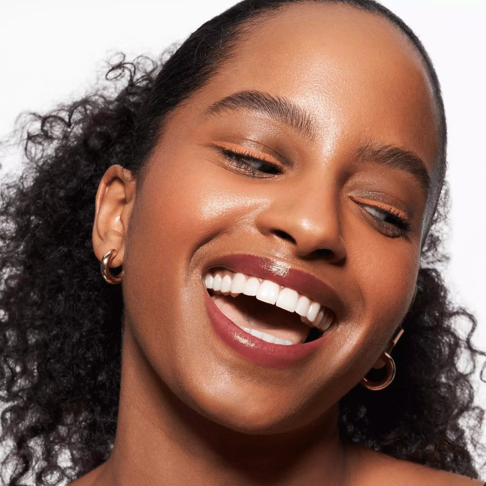 Femme à la peau bronzée avec trait de khôl. Elle porte des boucles d'oreilles dorées et du rouge à lèvres.