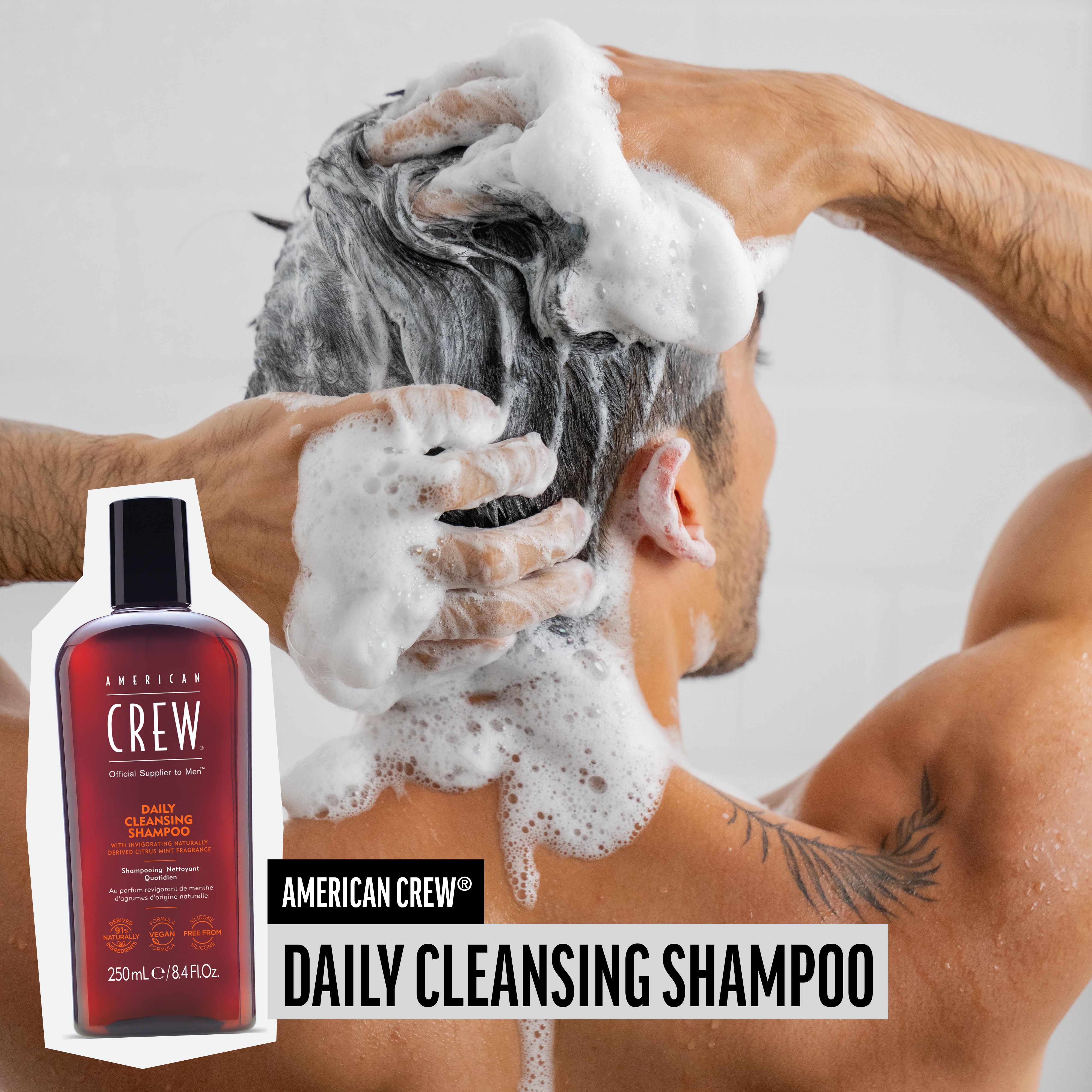 Man wast haar met schuim. AMERICAN CREW Daily Cleansing Shampoo fles in beeld.