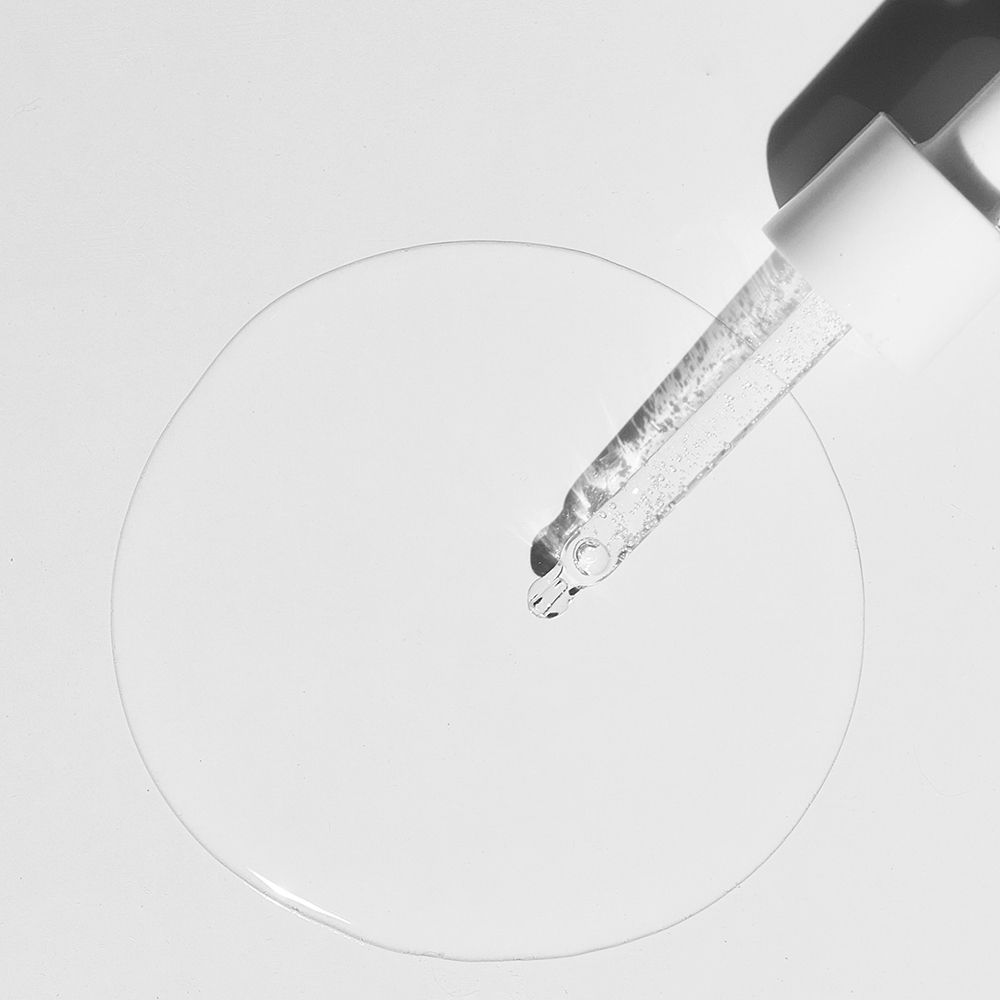 Pipet met vloeistof. Vloeistof druppelt op een cirkelvormig oppervlak. Witte achtergrond.