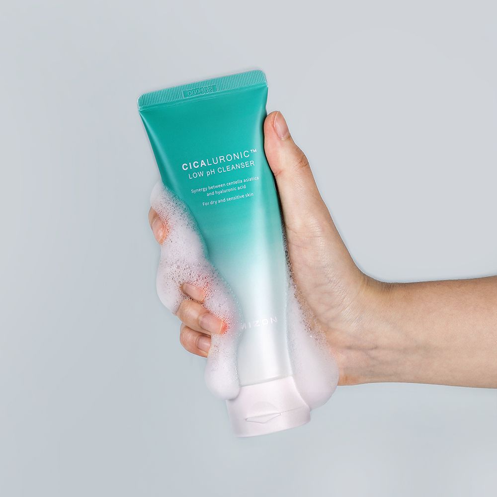 Een hand houdt een tube met productnaam. Schuim bedekt de hand en de tube. Groen-witte kleurstelling.