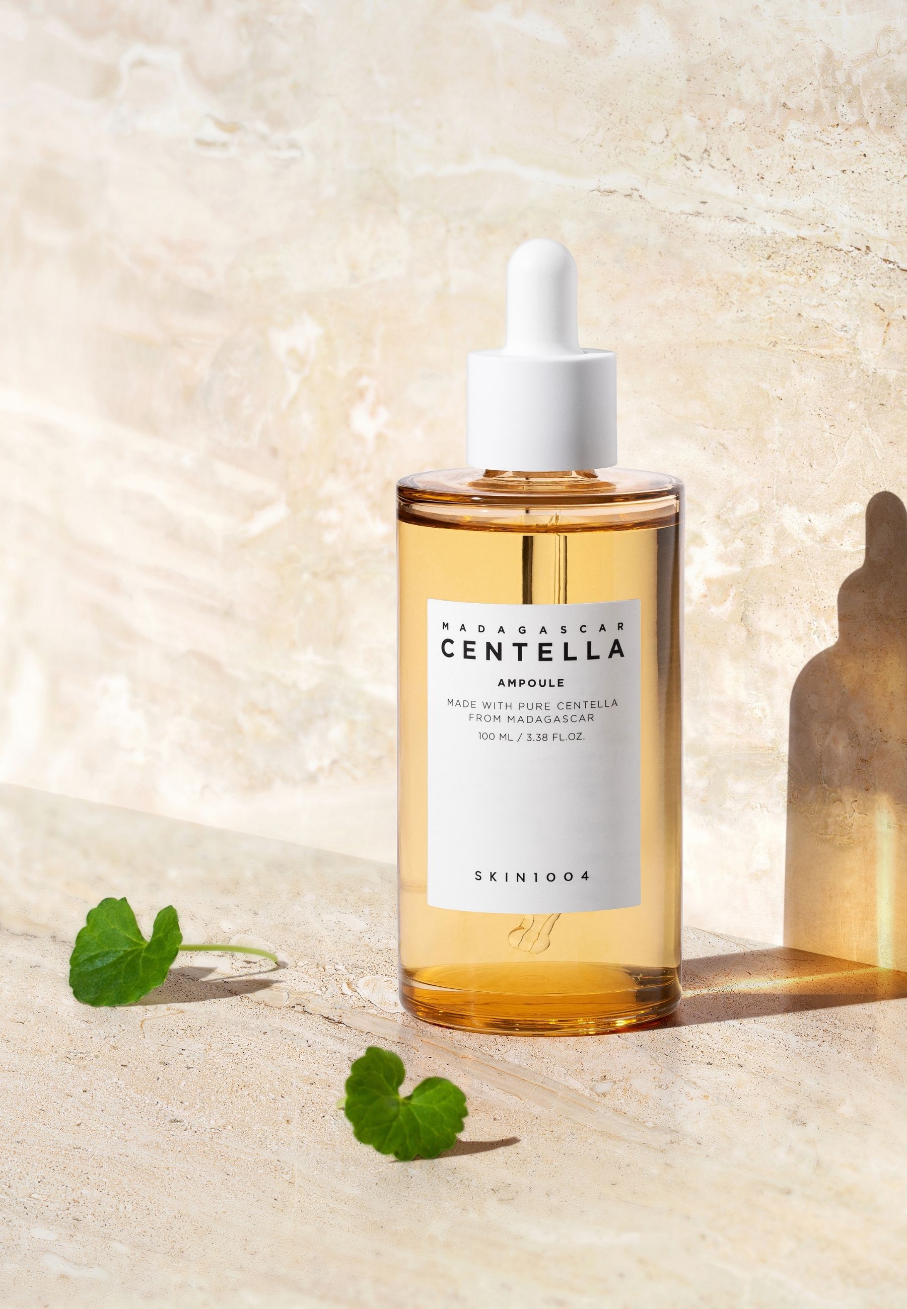 Glazen flesje met serum, witte dop en pipet. Opschrift: MADAGASCAR CENTELLA AMPULE. SKIN1004. Groene plant.