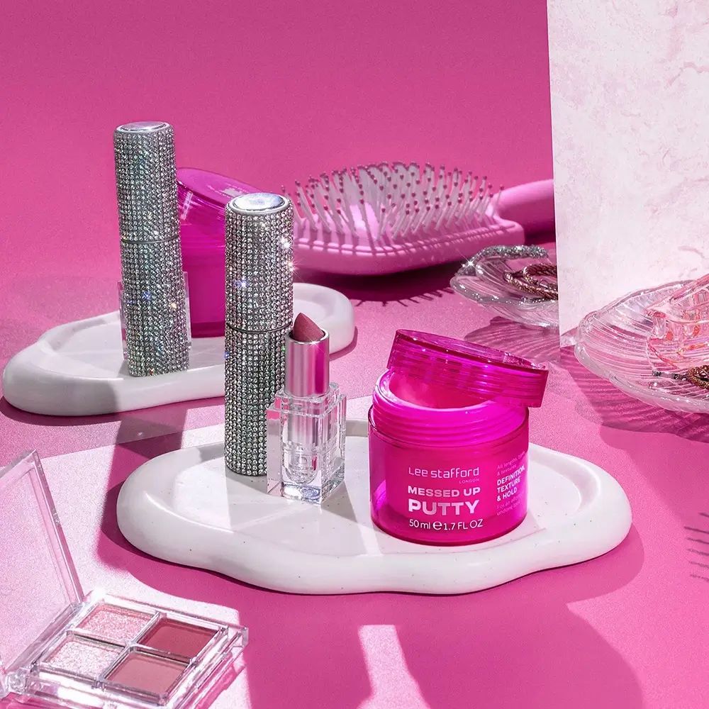 Roze cosmetica op trays: lippenstift, borstel, oogschaduw en "Messed Up Putty" van Lee Stafford.