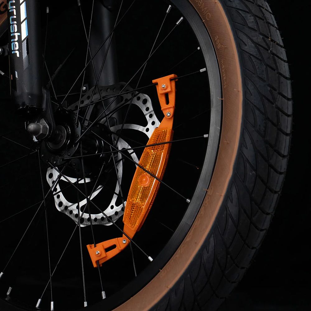 Gros plan sur un pneu de vélo avec réflecteur orange. Pneu noir, disque de frein visible.