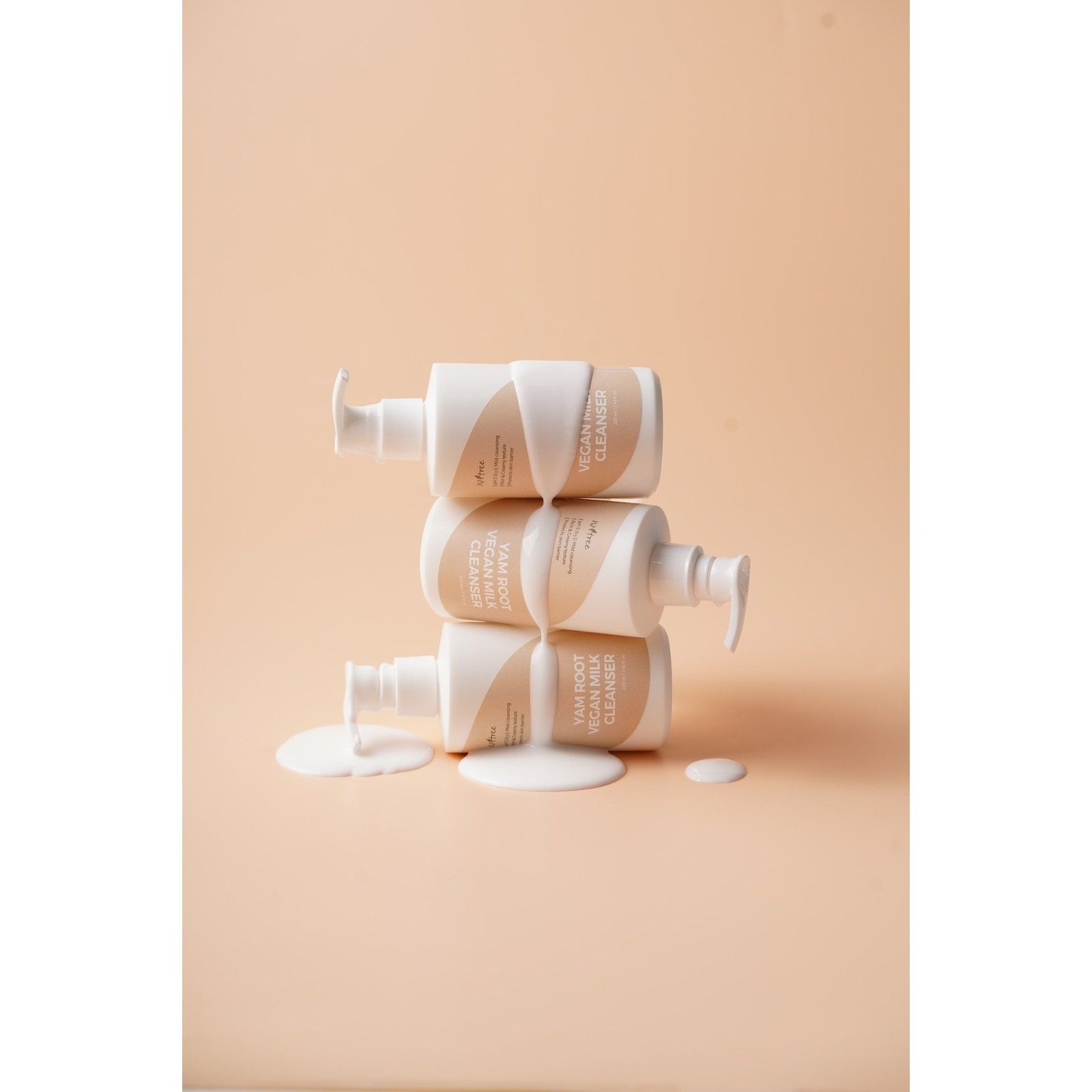 Trois flacons de nettoyant au lait végétalien à la racine d'igname empilés et recouverts de lait.