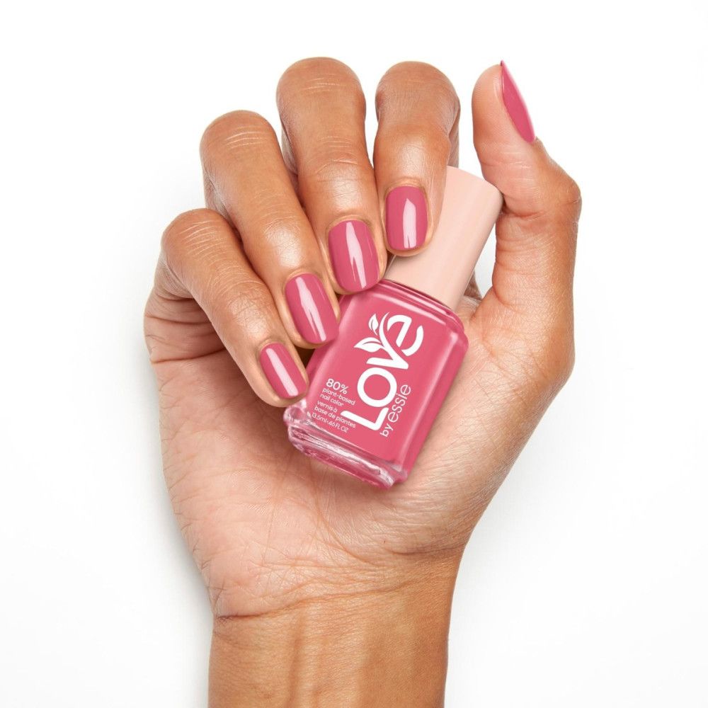 Hand met gelakte nagels en nagellakfles. Fles met roze nagellak, opschrift 'Love by essie'.