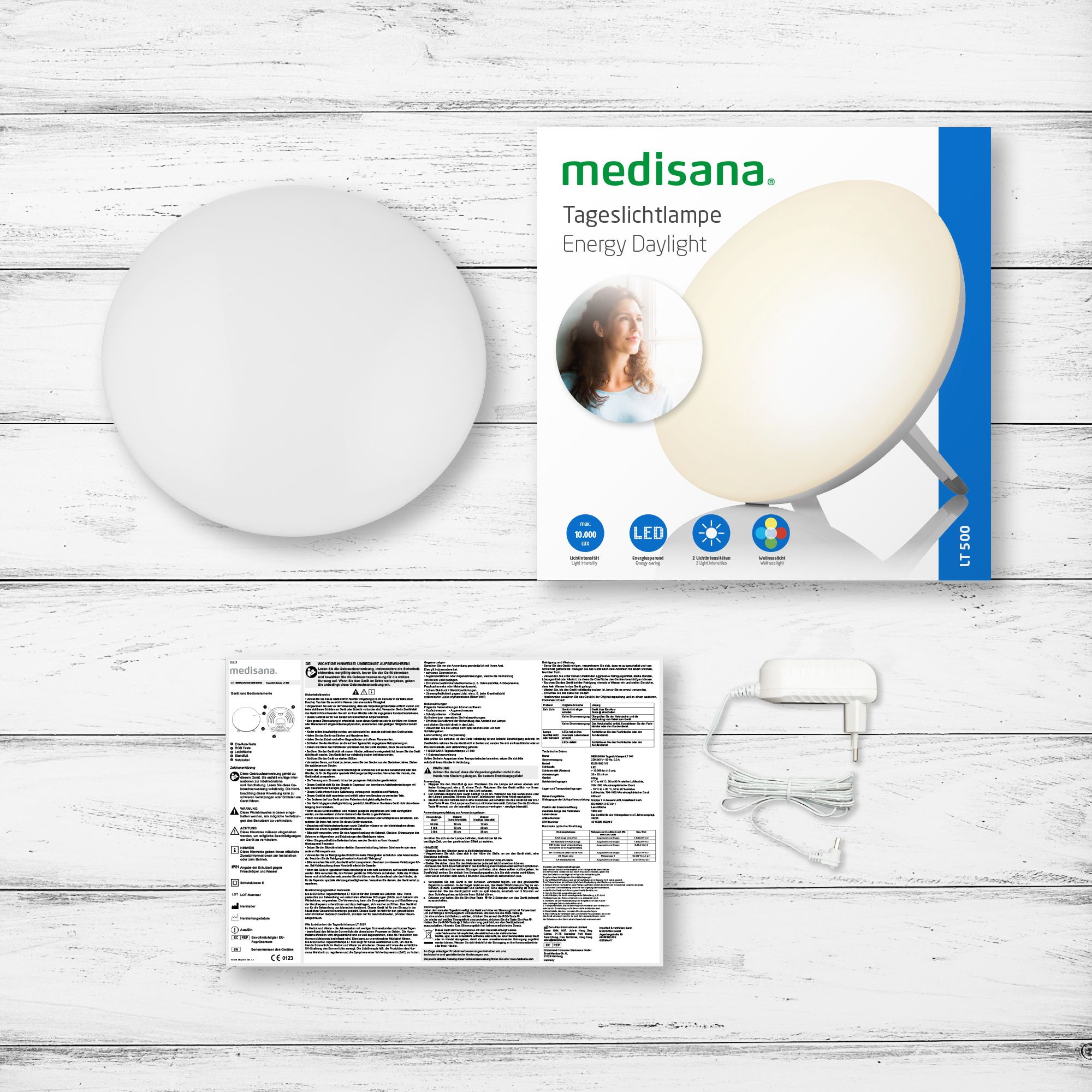 Verpakking van een medisana daglichtlamp met accessoires: lamp, adapter, handleiding.