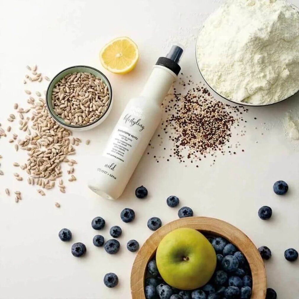 Flacon beige avec vaporisateur noir, entouré d'ingrédients : graines de tournesol, myrtilles, citron, pomme, poudre.