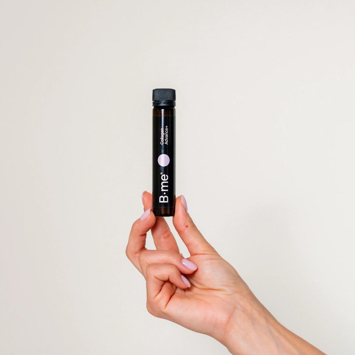 Une ampoule marron B.me® Collagen Advance+ tenue par une main. Bouchon noir, point rose et texte sur l'ampoule.