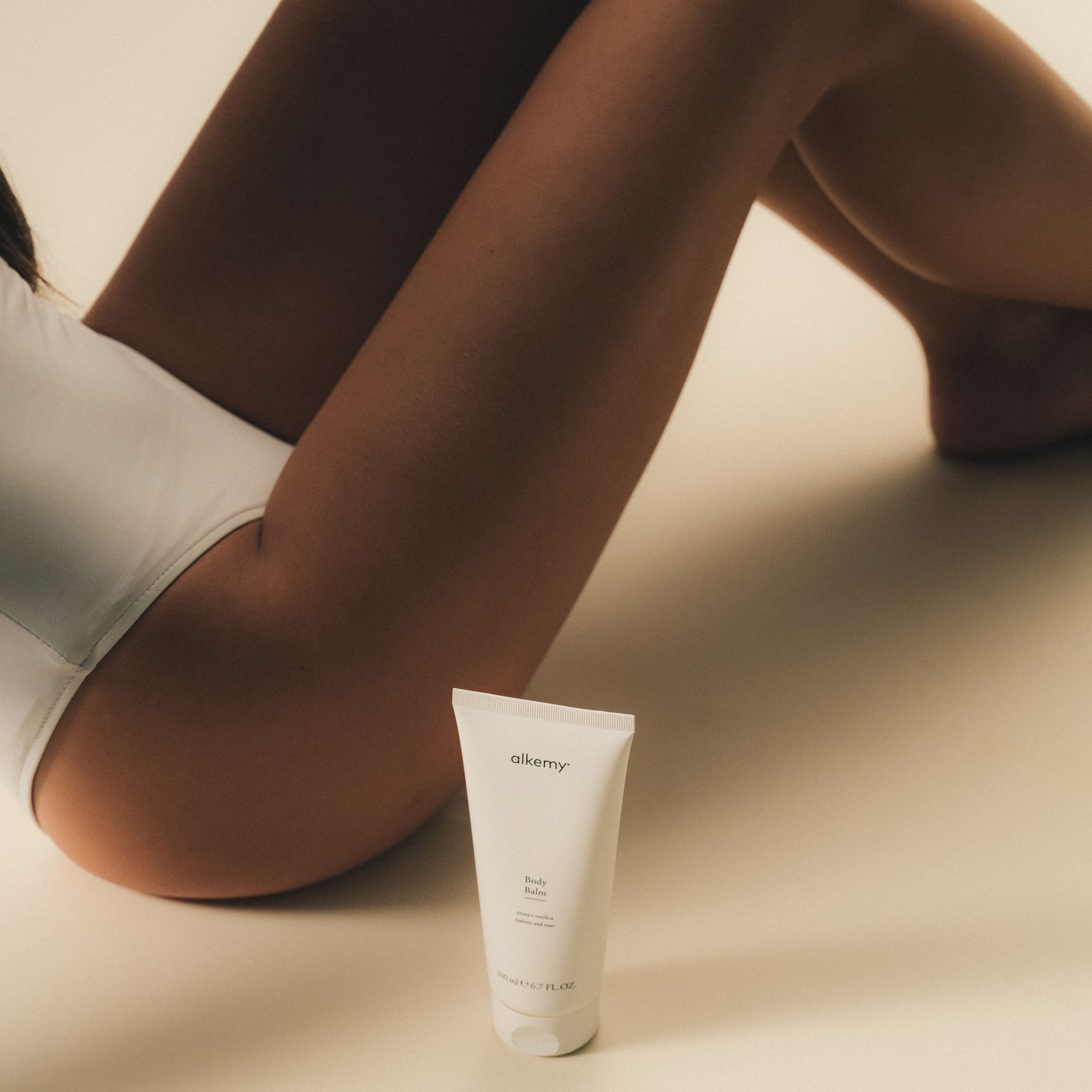 Un tube blanc de baume corporel posé au sol à côté des jambes d'une personne.