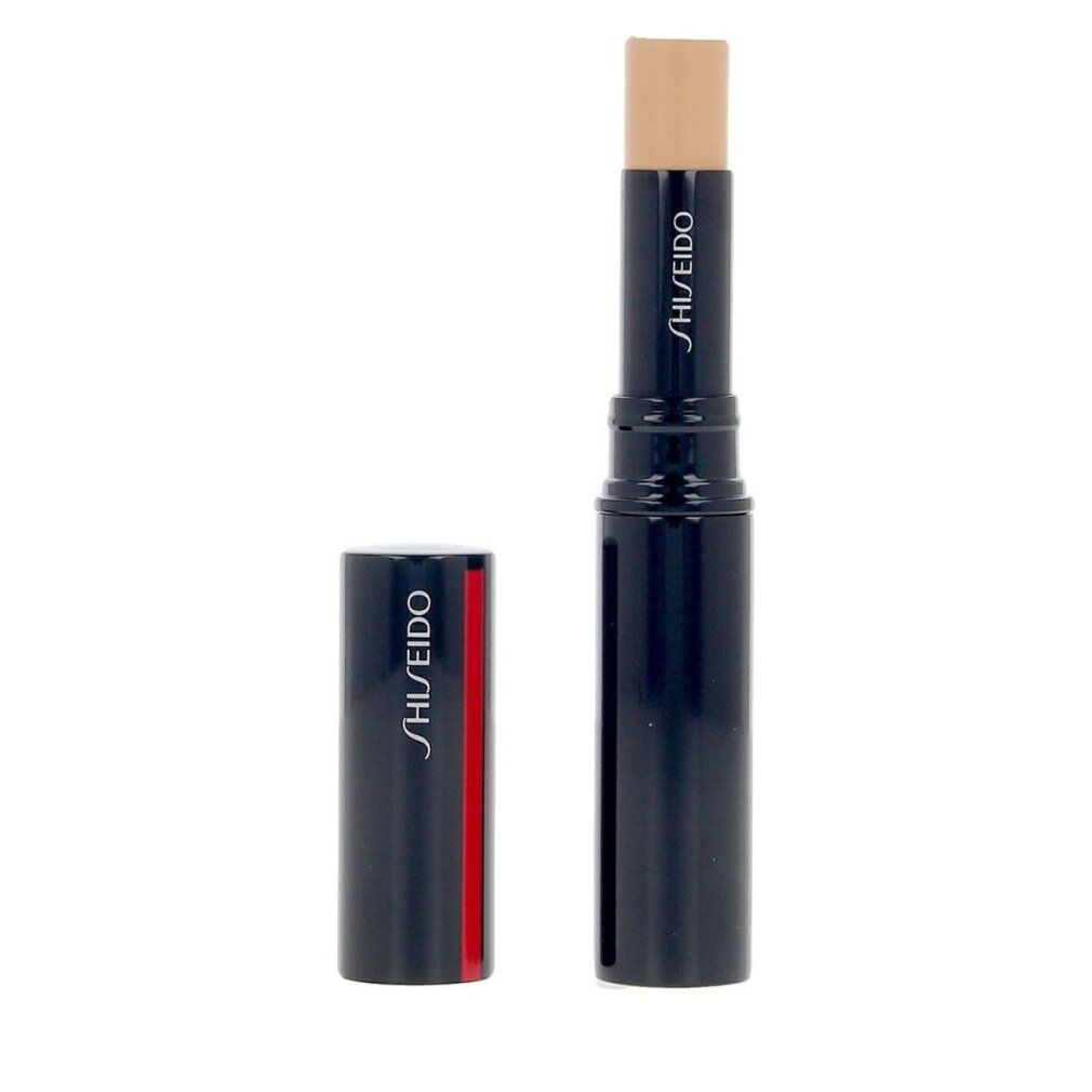 Stick correcteur, bleu foncé avec rayure rouge. Capuchon à côté. Nom du produit et marque: SHISEIDO. Stick couleur crème.