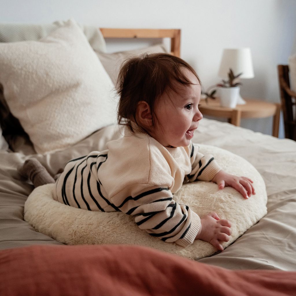 Bébé allongé sur un lit, sur un coussin crème. Bébé porte des vêtements rayés.