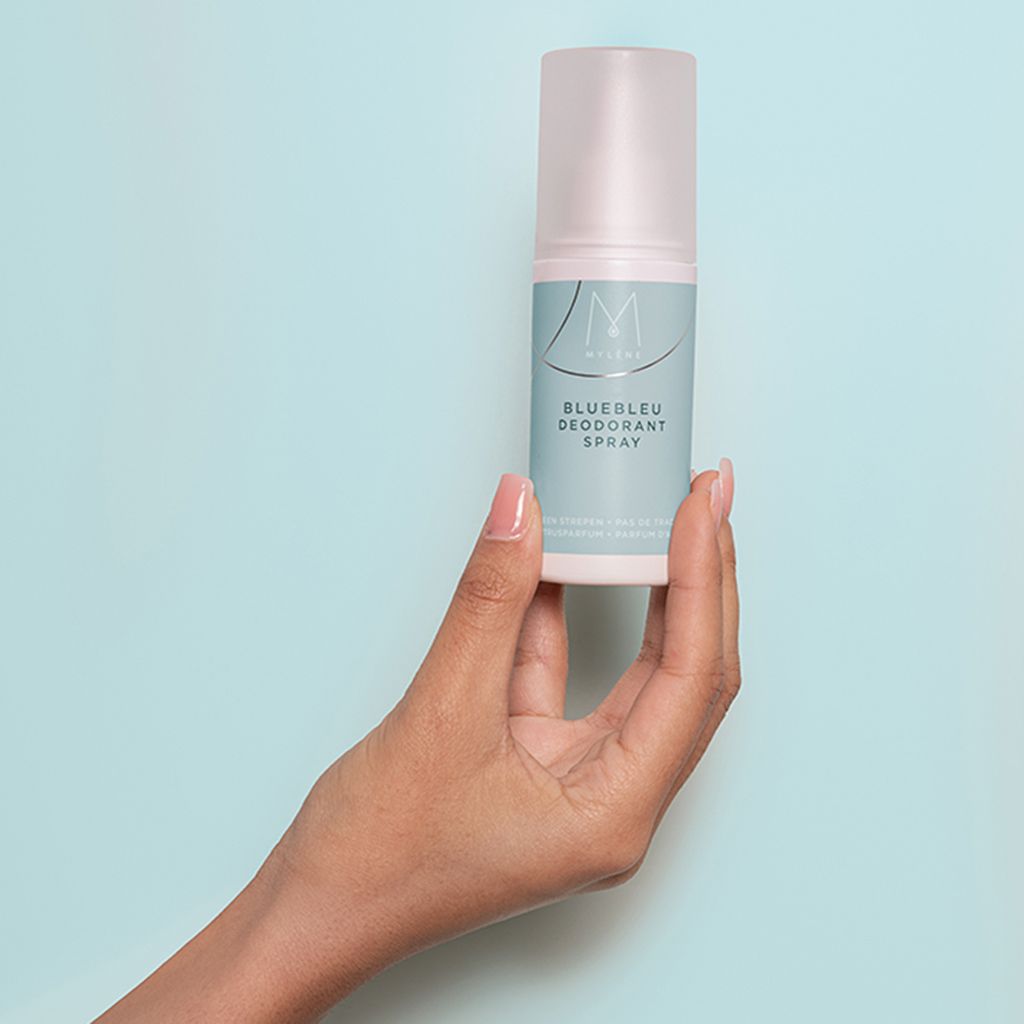 Une main tient un flacon de spray déodorant Mylène Bluebleu.