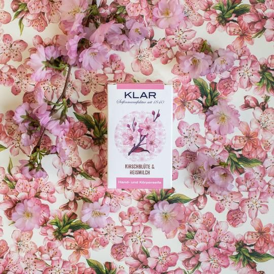 Klar zeepverpakking omringd door kersenbloesem. Verpakking: wit met roze accenten, illustratie van kersenbloesem. Opschrift: Kirschblüte & Reismilch.
