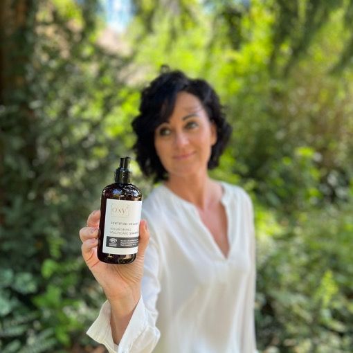 Une femme tient un flacon de shampooing. L'étiquette indique "oxy8" et "Nourishing Multicare Shampoo".