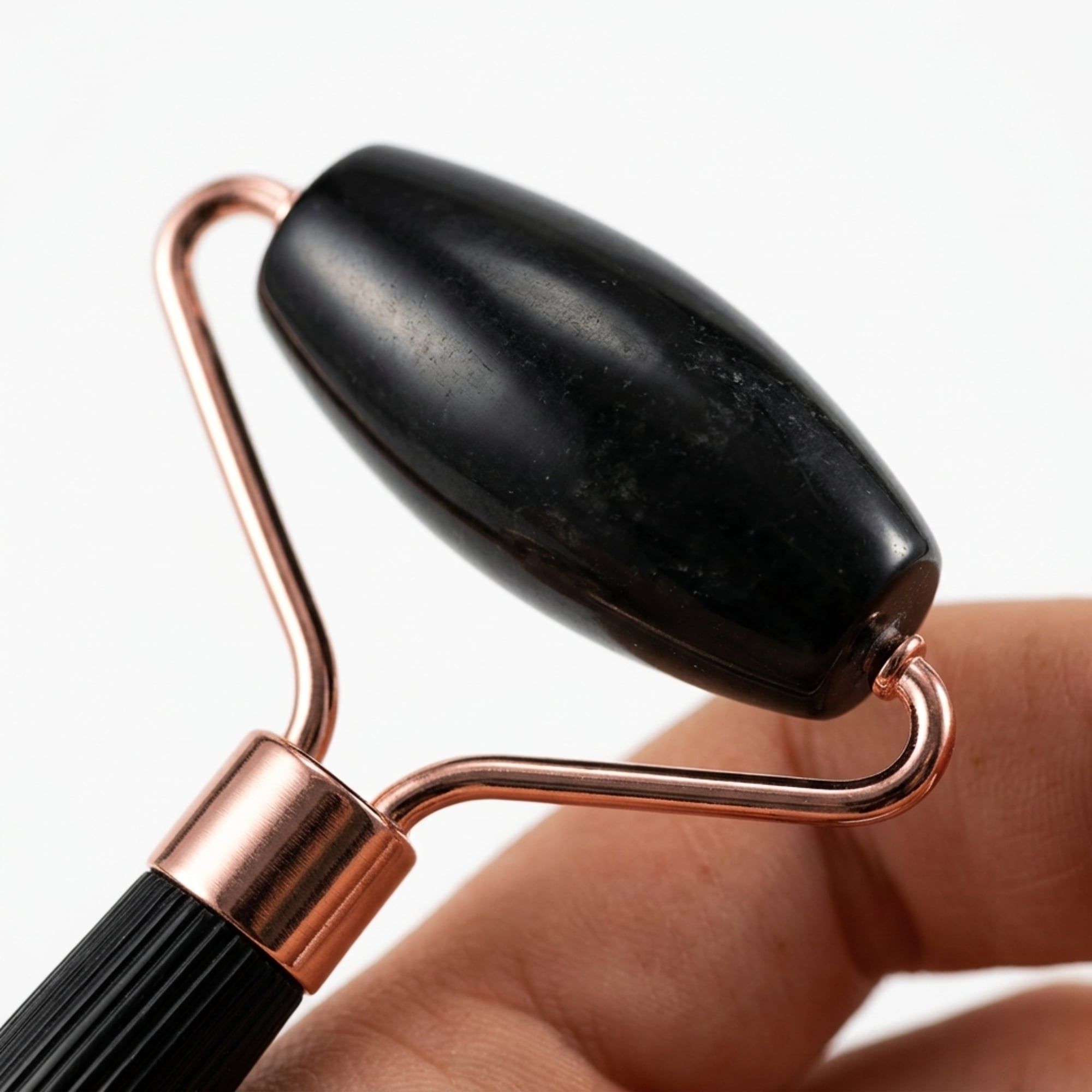 Zwarte jade roller met koperkleurig metalen frame, vastgehouden door een hand.