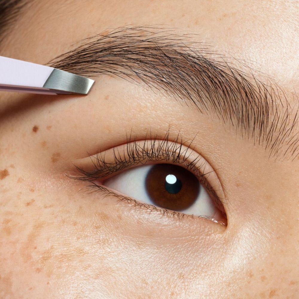 Gros plan sur un œil avec sourcils. Pince à épiler en cours d'utilisation.