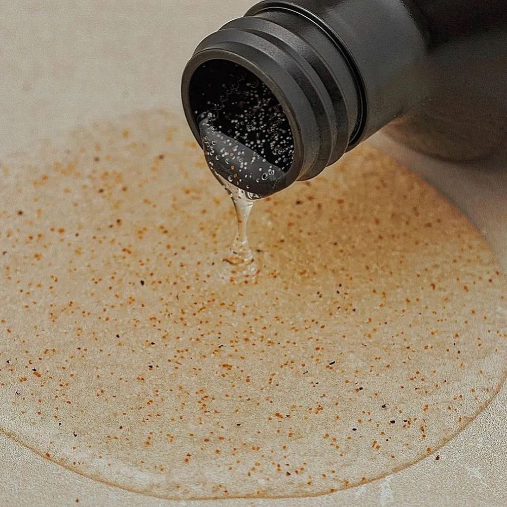 Flacon brun avec pompe noire. Liquide versé sur une surface. Aucune indication de produit visible.