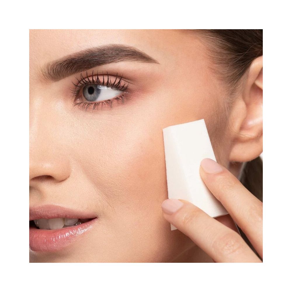 Une femme utilise une éponge de maquillage triangulaire sur sa joue.