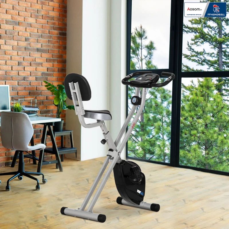 Hometrainer in een kamer. Ramen, bureau, stoel en bakstenen muur zichtbaar.